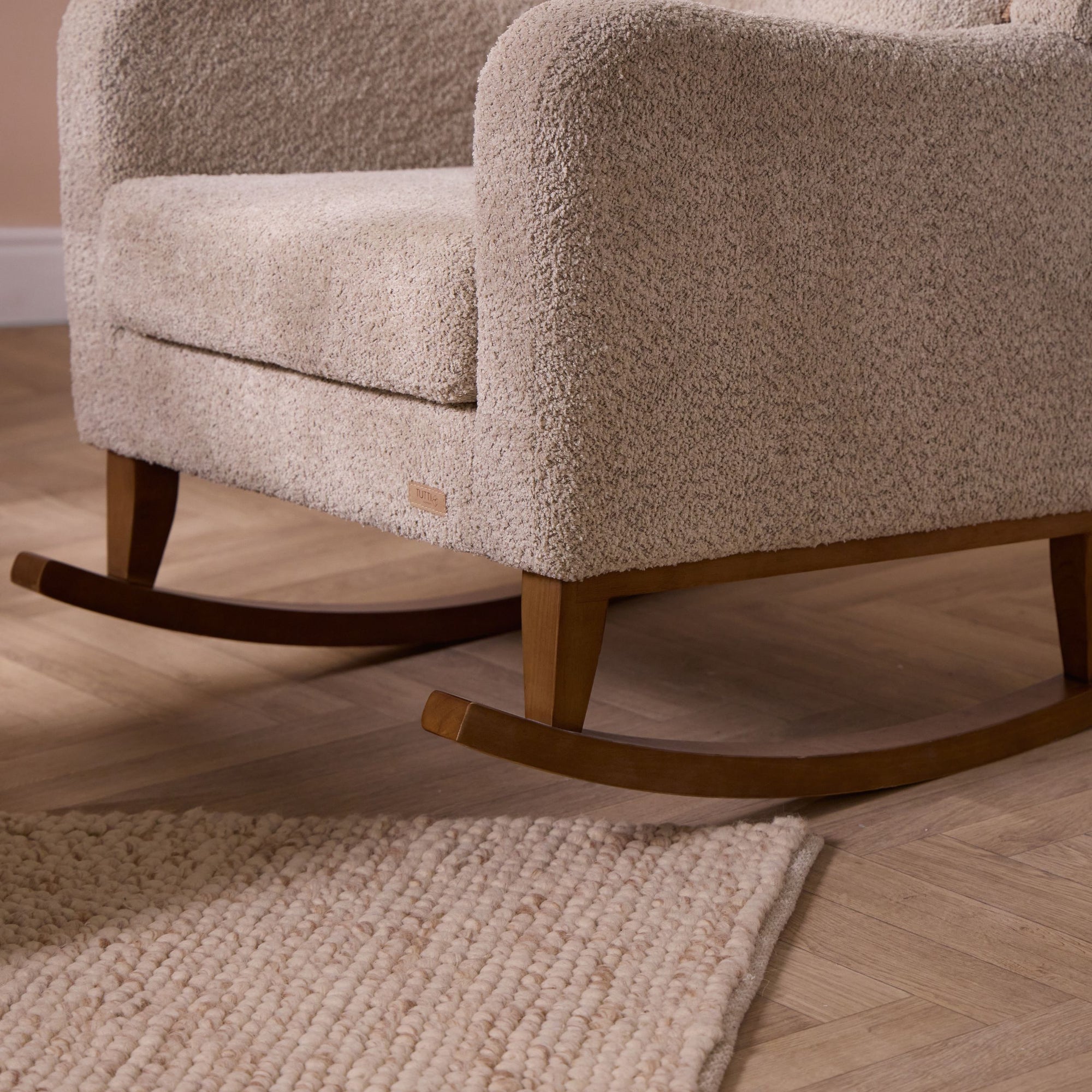 Beige textured rocking chair with wooden legs on a wooden floor with a rug.