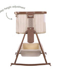 An infographic of a baby bedside crib on a rocking stand with a beige striped fabric body, brown frame, and a built-in height adjustment dial on the front. An arrow indicates the '6 step height adjustment'.