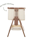 An infographic of a bedside crib with a cream striped fabric and brown wooden frame and legs, shown on a white background. The text points to a '6 step height adjustment' highlighting the height adjustment mechanism.