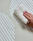 Hand wiping water off the oatmeal and white Oddity Infinity Playmat, highlighting its easy-to-clean surface.