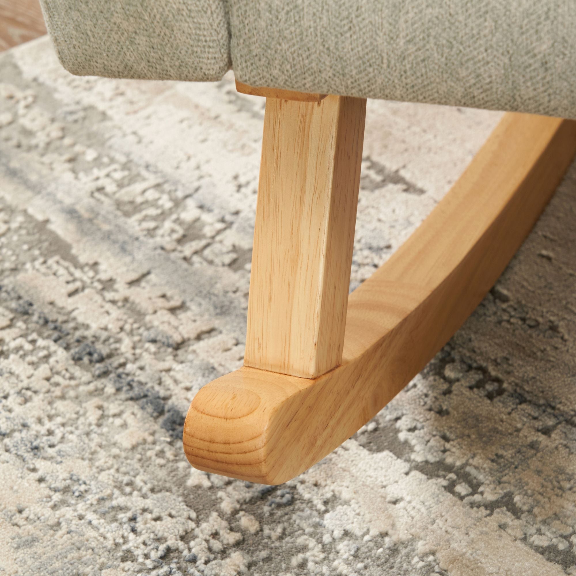 Close up of the Jonah rocking chair leg placed in a blue and beige rug