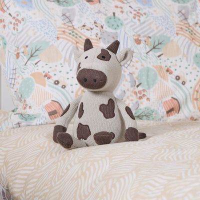 Plush cow toy on a patterned bedding in a bed