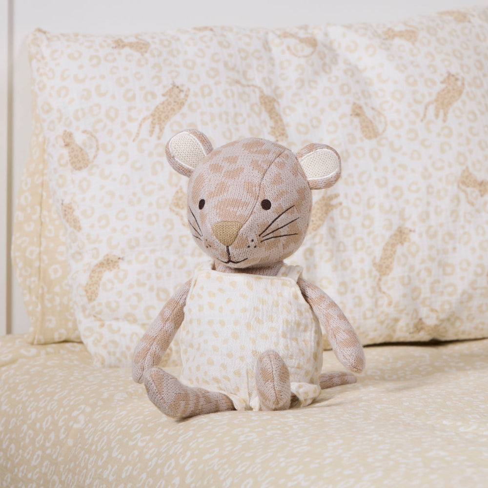 A plush stuffed leopard toy sits centered on a bed with matching patterned bedding and pillows in the background.