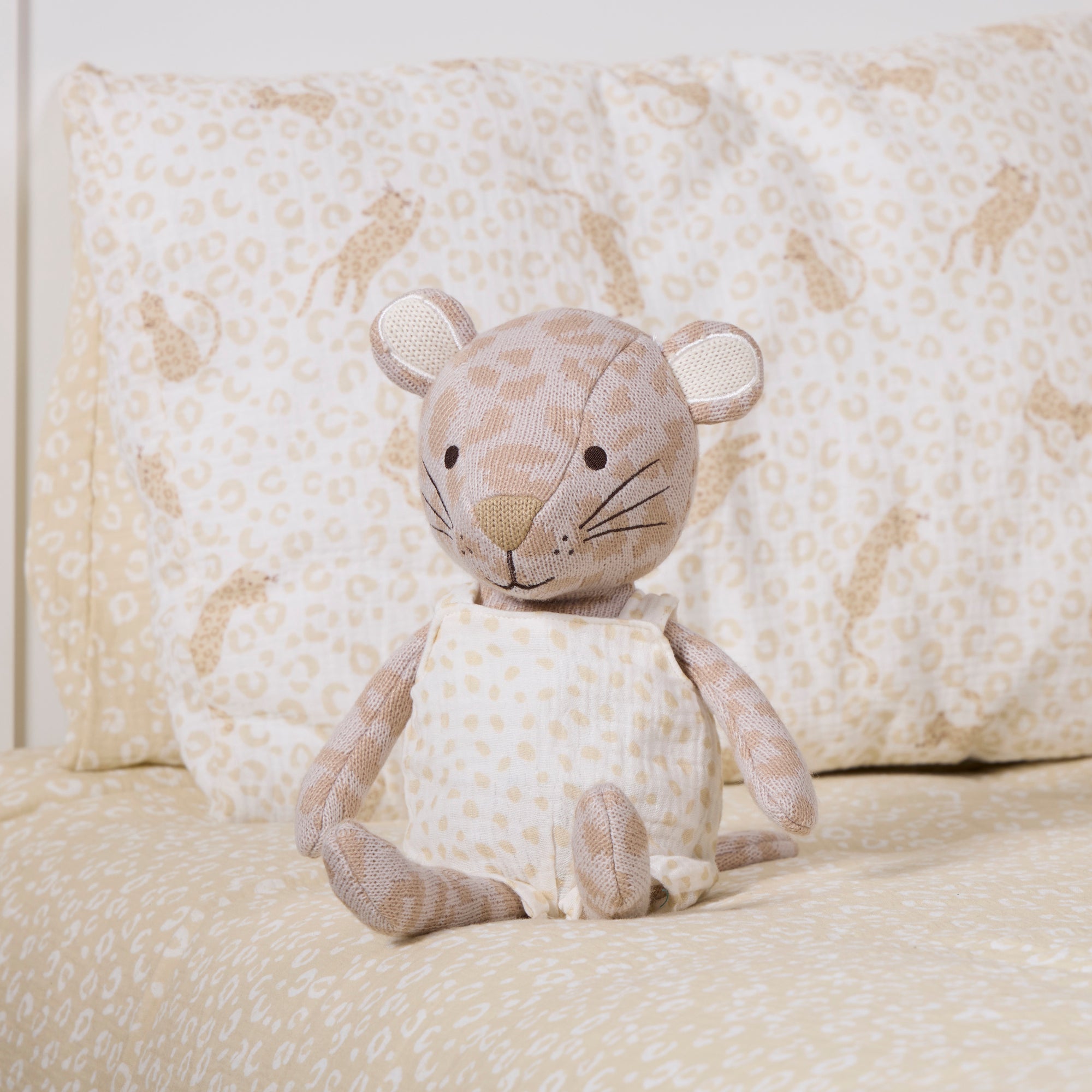 A plush stuffed leopard toy sits centered on a bed with matching patterned bedding and pillows in the background.