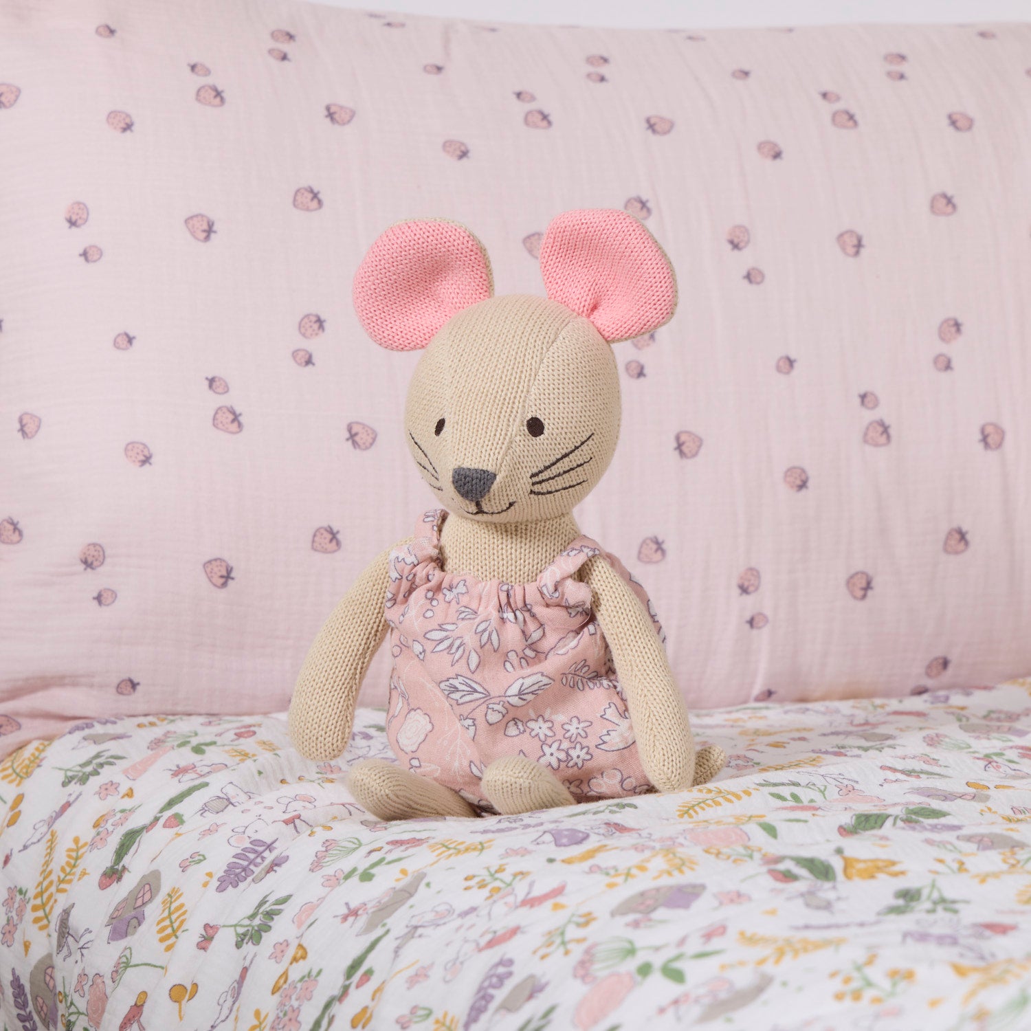 Margot Mouse knitted toy sitting on a floral-patterned bedspread with a pink background.