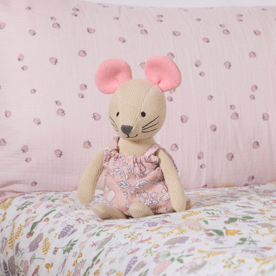 Margot Mouse knitted toy sitting on a floral-patterned bedspread with a pink background.