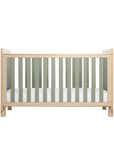 A Scandi-style cot bed with rounded corners, sturdy block legs, sage weave texture on the ends and slats, and a pickled oak frame on a white background.