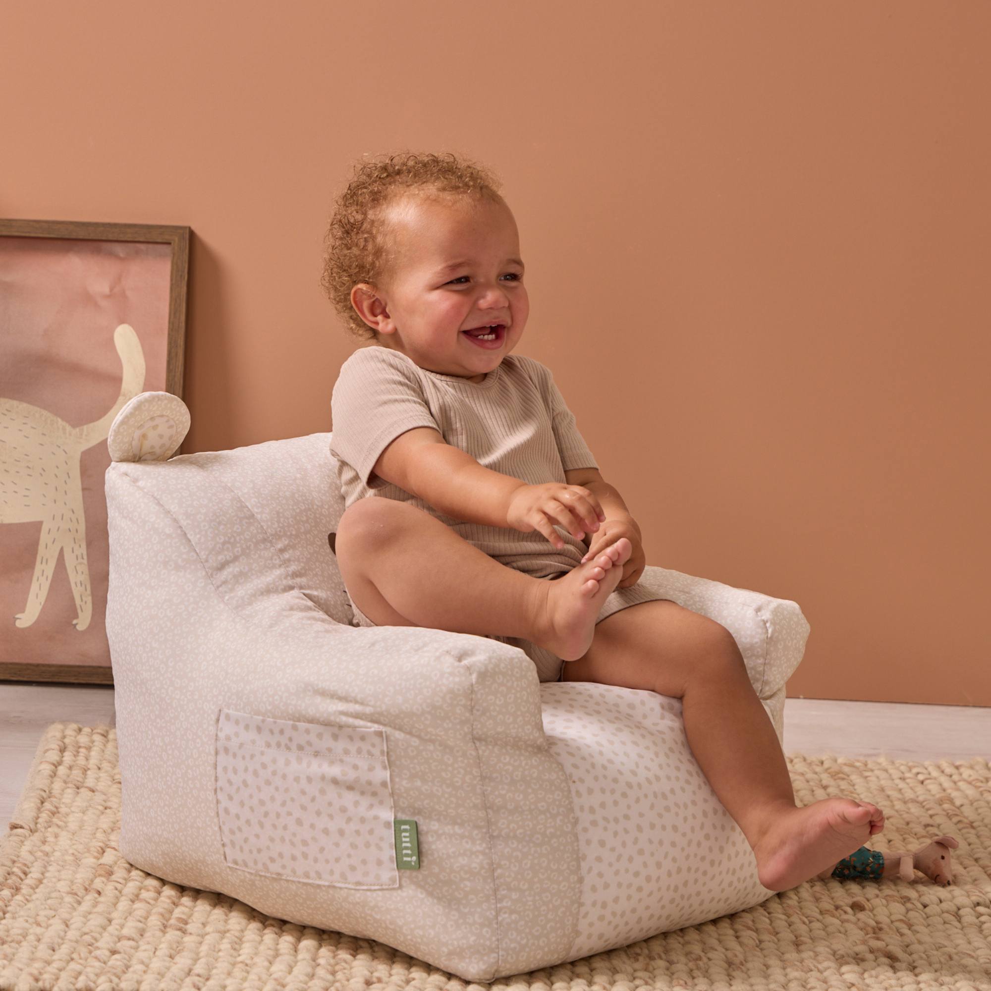 A child is sitting on the Larry Leopard beanbag chair in a room with beige walls and a framed picture.
