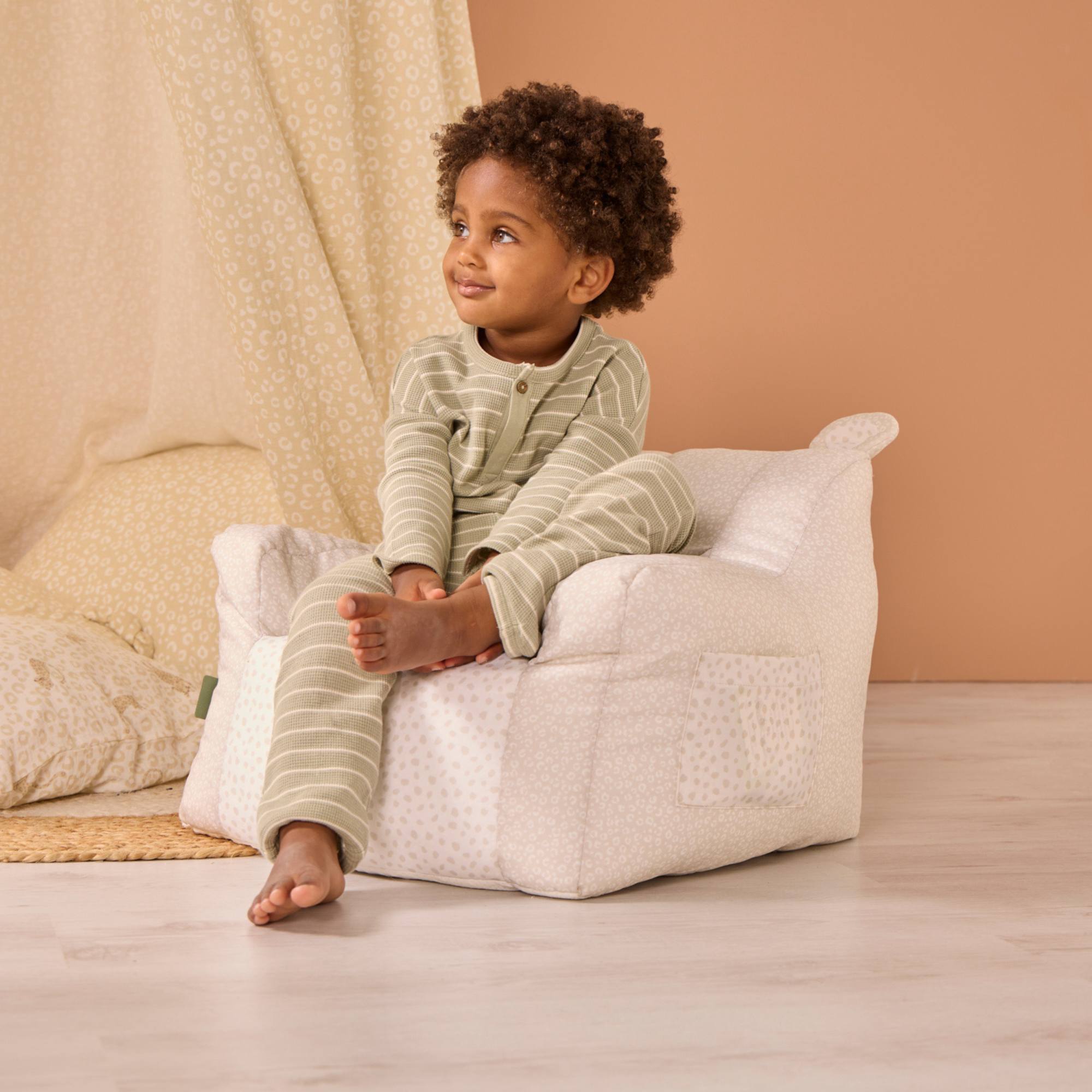 Child sitting on the Larry Leopard beanbag with beige leopard print design on a wooden floor