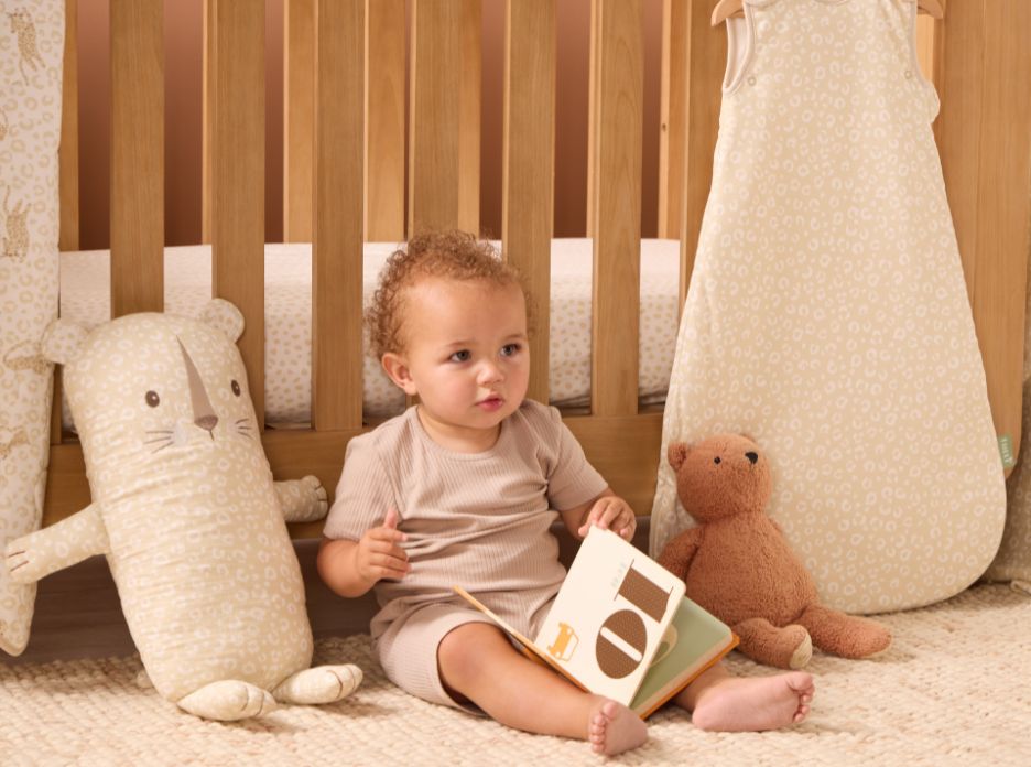 Toddler sitting on rug beside wooden cot, styled with larry leopard cushion and matching bear cushion.