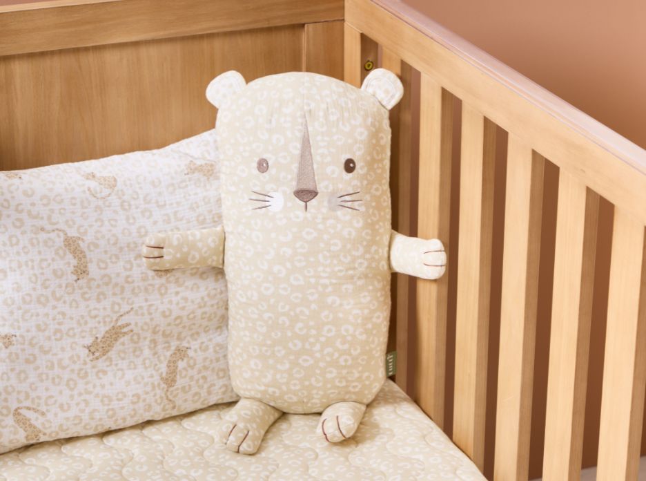 Neutral larry leopard print bear cushion styled inside wooden cot, paired with coordinating fitted sheet and quilted bedding.
