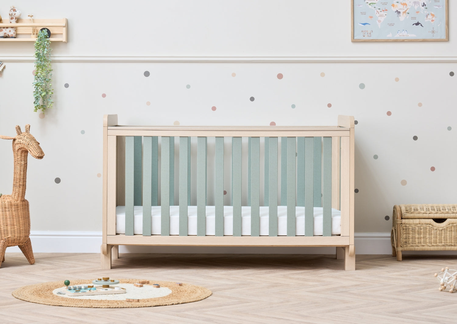 Room view of the Kuba cot bed in pickled oak with sage weave slats, showcasing clean lines and a calm, softly styled nursery setting