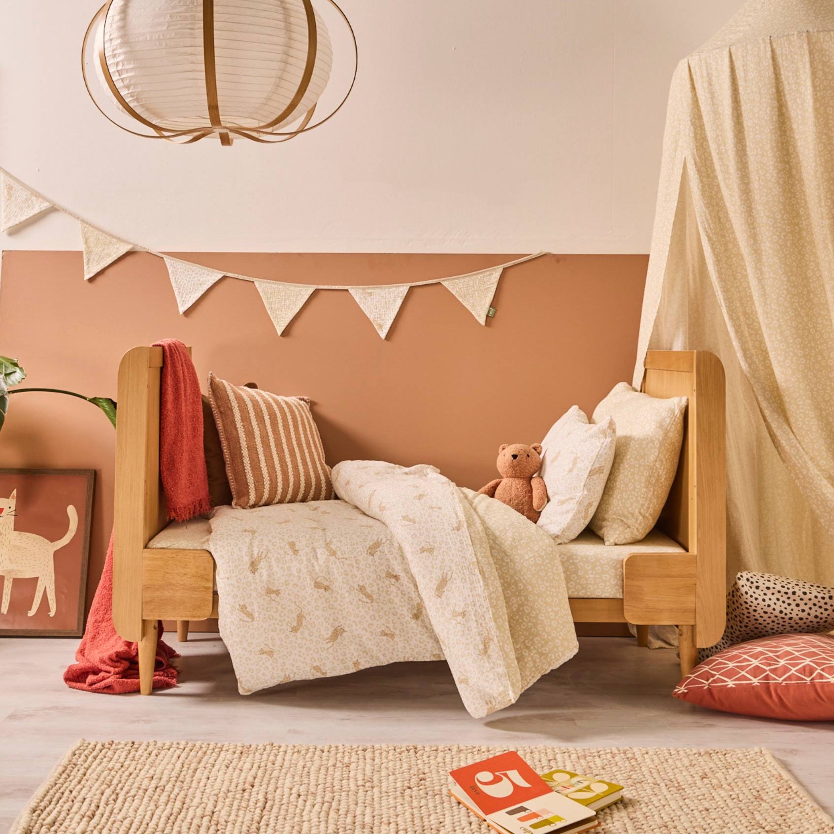Children's bedroom with a wooden cot bed in toddler-bed mode with Love Cats duvet cover and pillows, and a teddy bear.