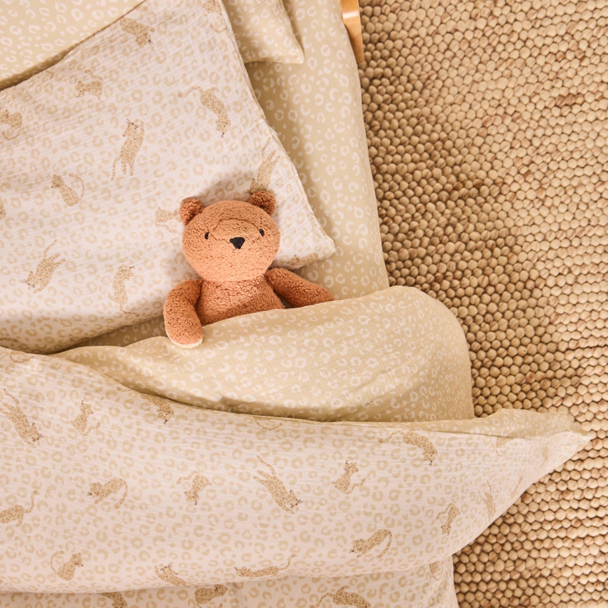 Brown teddy bear on a cot bed styled with the Love Cats bedding range in a beige animal print design