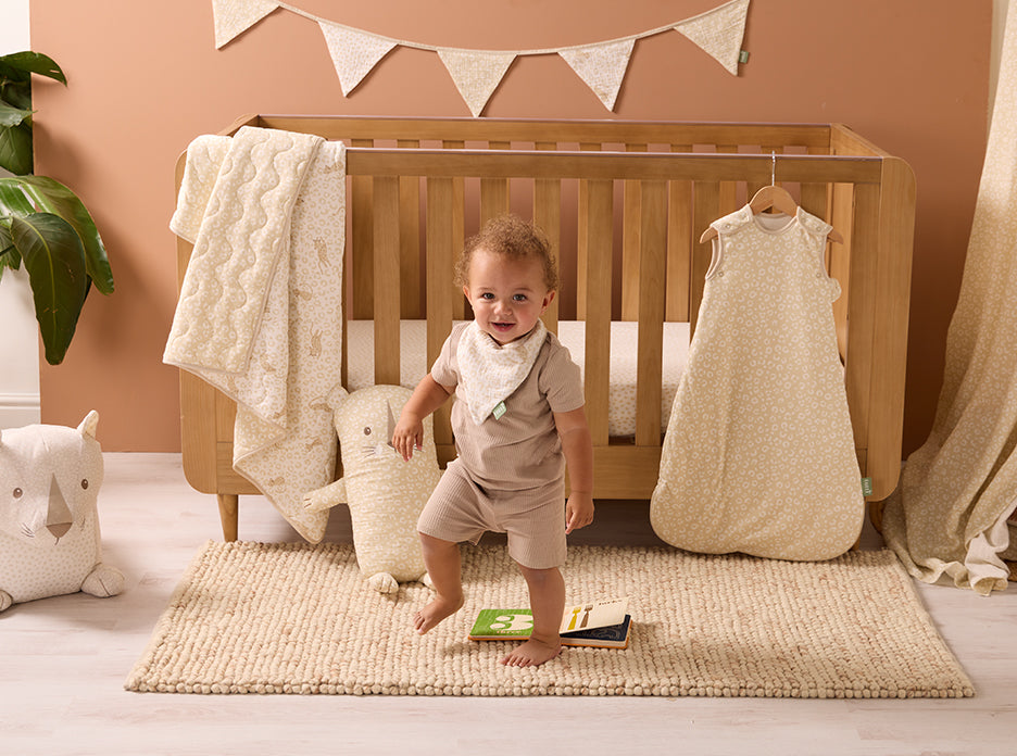 Child standing in a nursery with a cot bed and the bedding and soft toys of the Love Cats Collection.