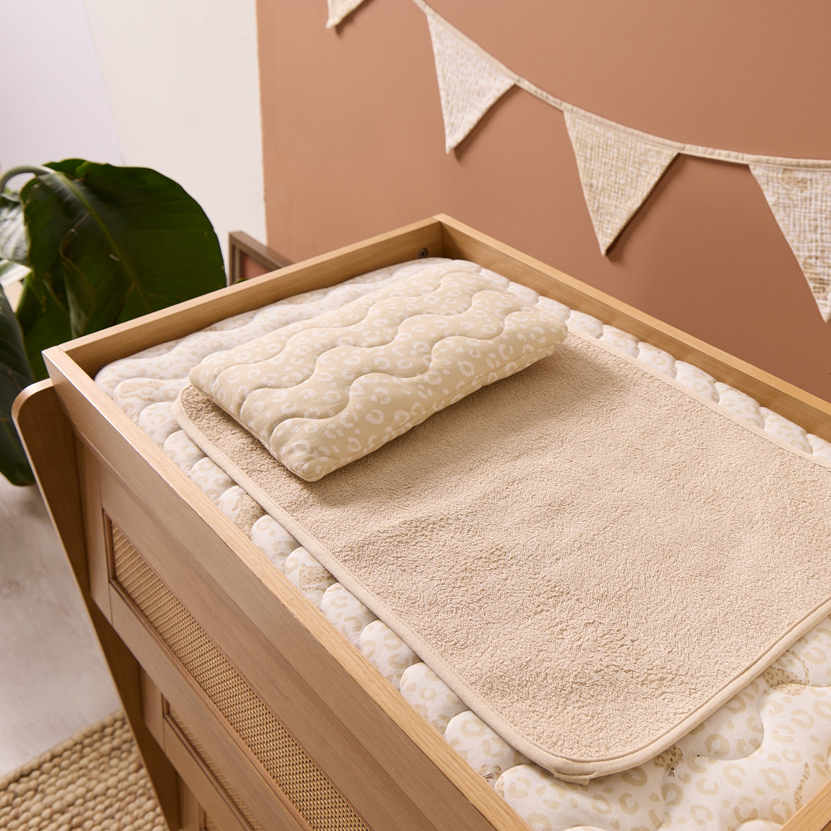 Love Cats luxury changing mat with textured surface on the chest changer, with a plant and decorative flags in the background.
