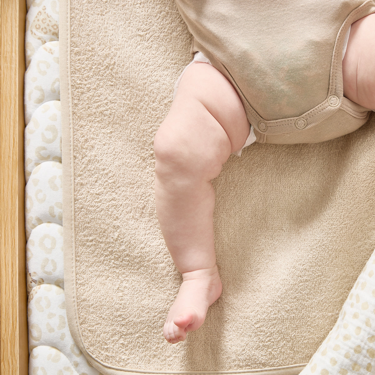Baby's legs on a textured beige mat with a wooden side.