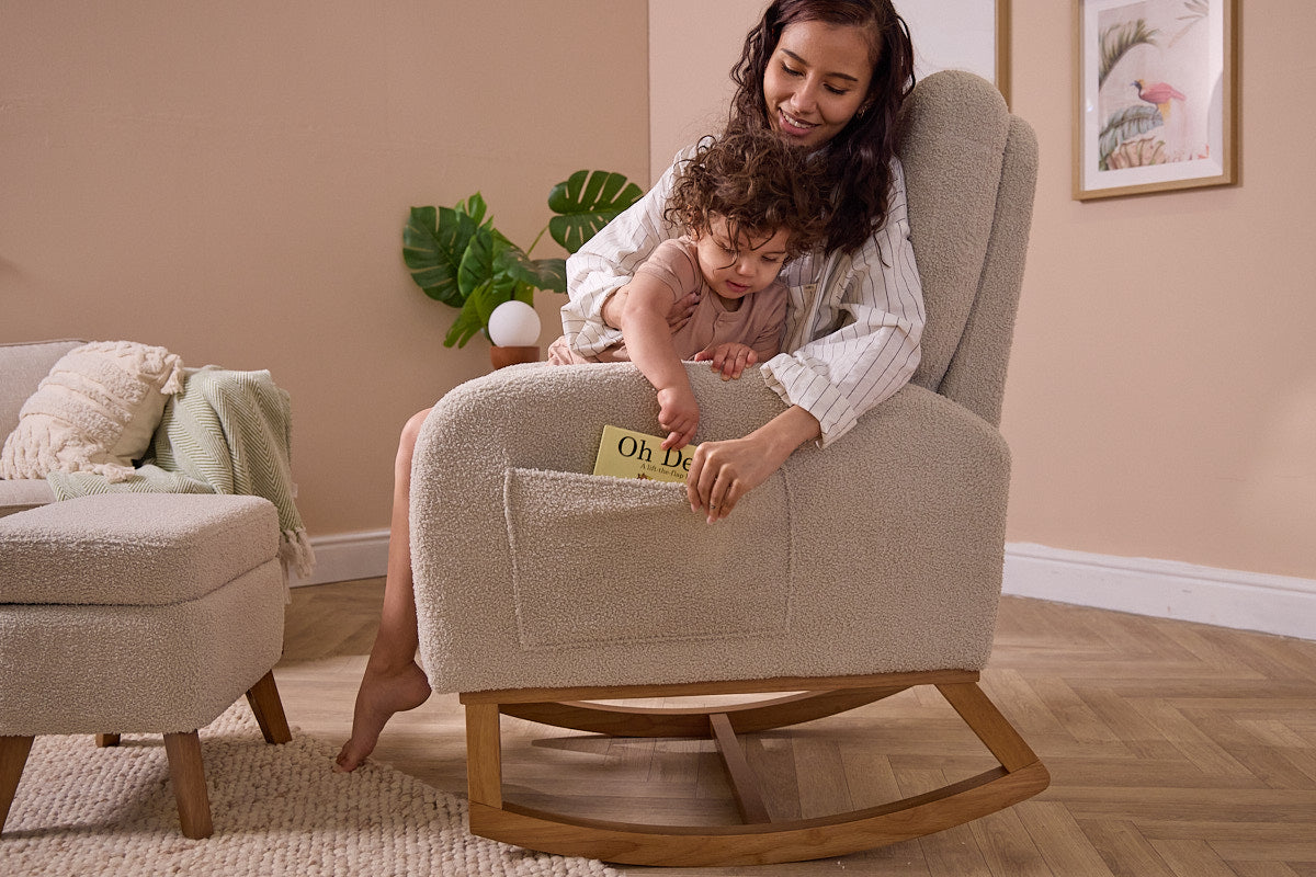 A woman and child are placing a book in the side pocket of the Luca nursing chair