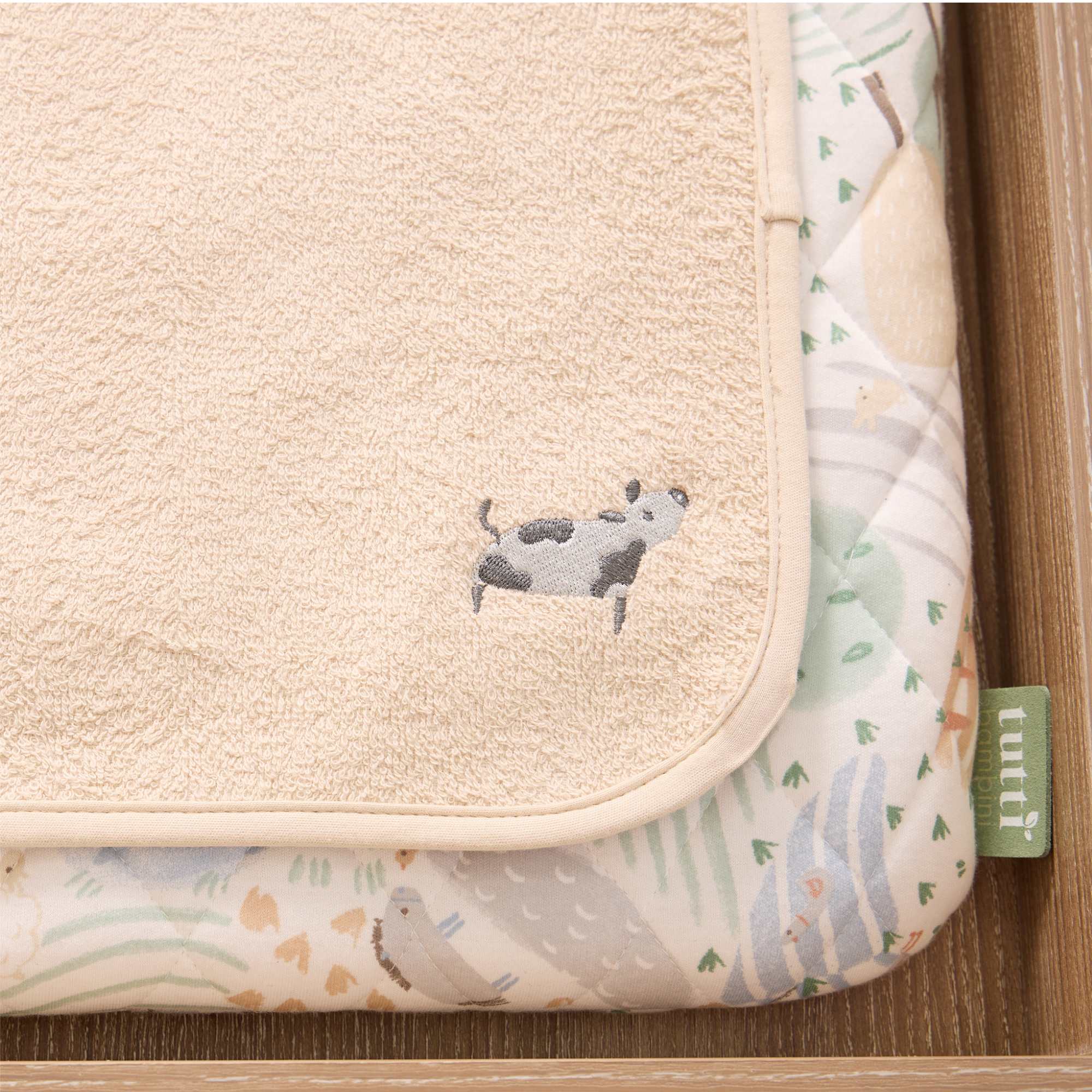 Detail of luxury changing mat with embroidered cow design and Tutti Bambini branding on a chest changer