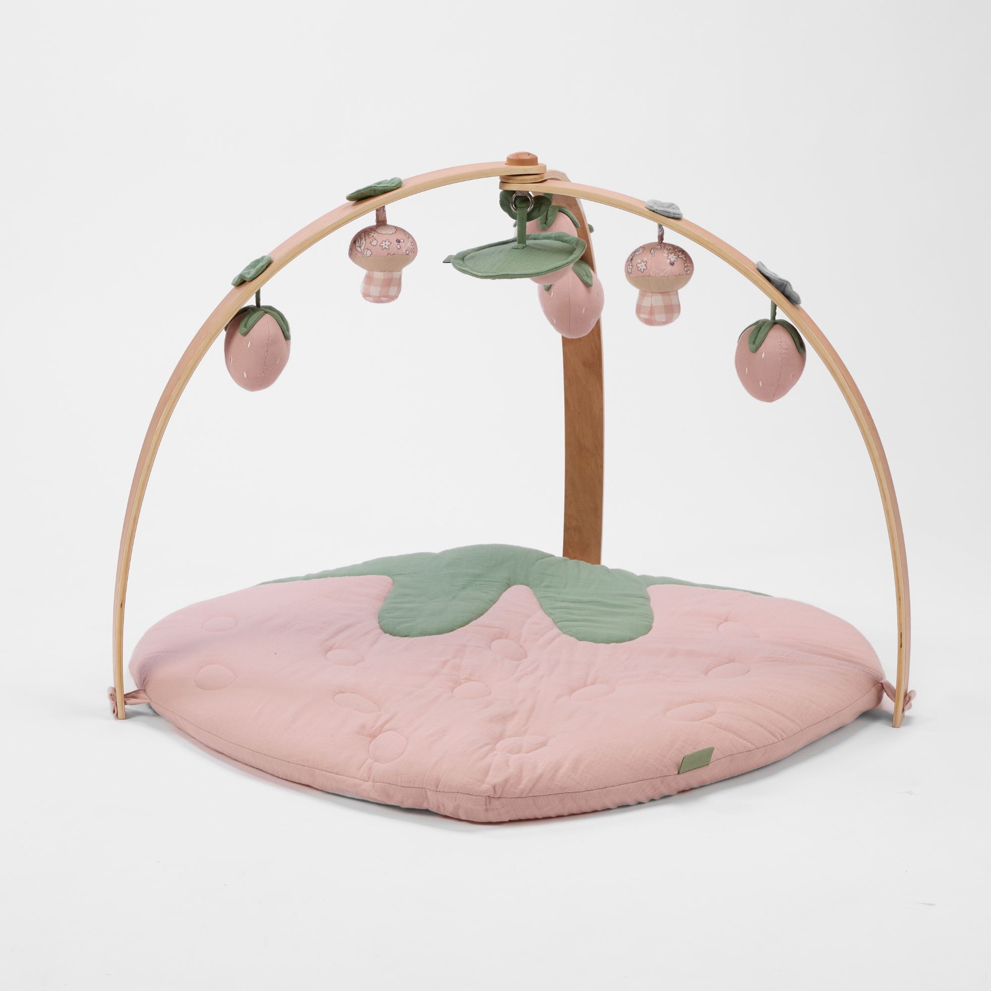 Strawberry-shaped muslin padded playmat with wooden arch playgym and hanging strawberry and mushroom toys.