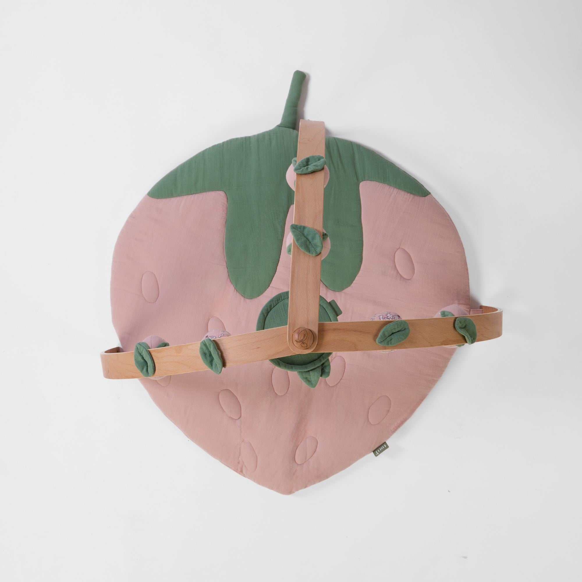Top-down view of strawberry-shaped padded muslin playmat with wooden playgym arch and leaf details.