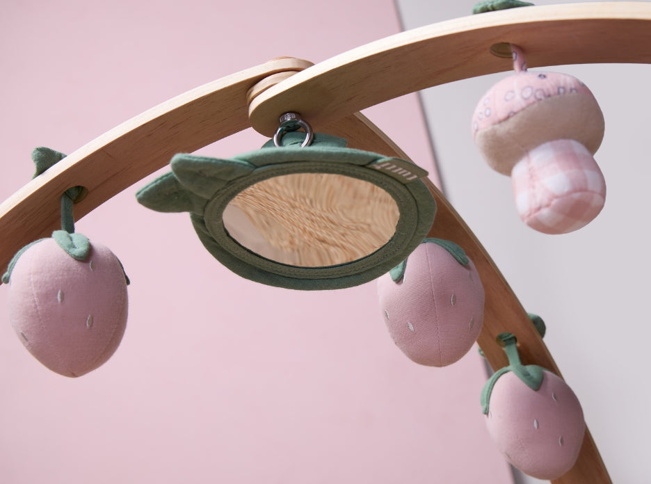 Close-up of leaf-framed sensory mirror with strawberry and mushroom hanging toys on wooden playgym arch.