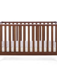 The Malmo cot bed in rich walnut with a mattress in a white background.