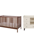 A cot bed in dark brown walnut wood and a changing table in a cream colour finish, shown on a plain white background.