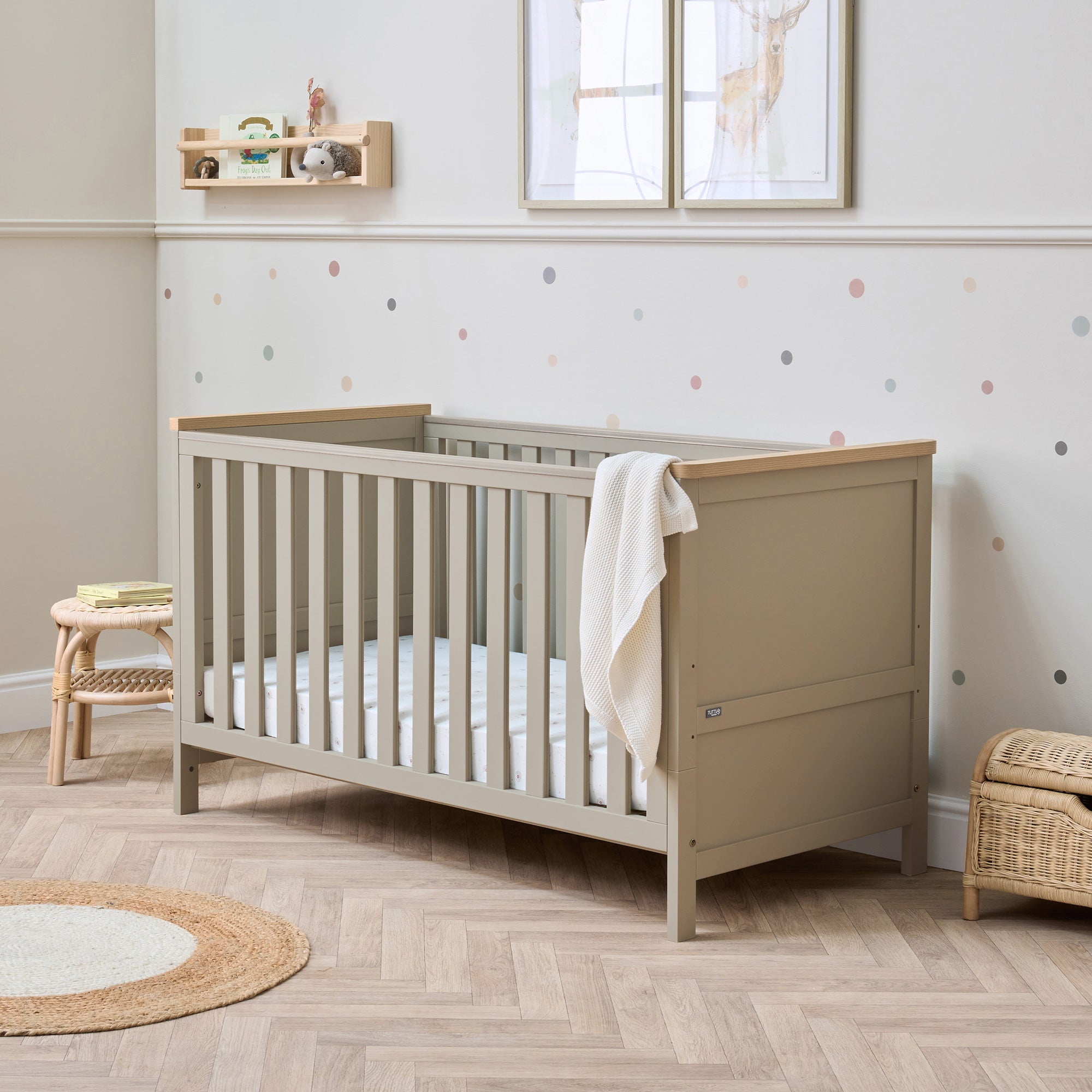 A Misha Cot Bed in Mushroom and Golden Oak colour, situated in a nursery room with a dotted wall.