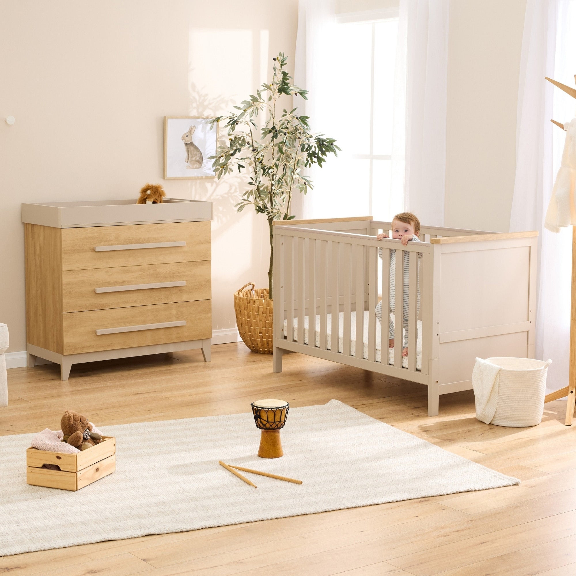 Misha cot bed and Hallee chest changer in mushroom and golden oak styled together in a bright, softly layered nursery space with toddler in cot.
