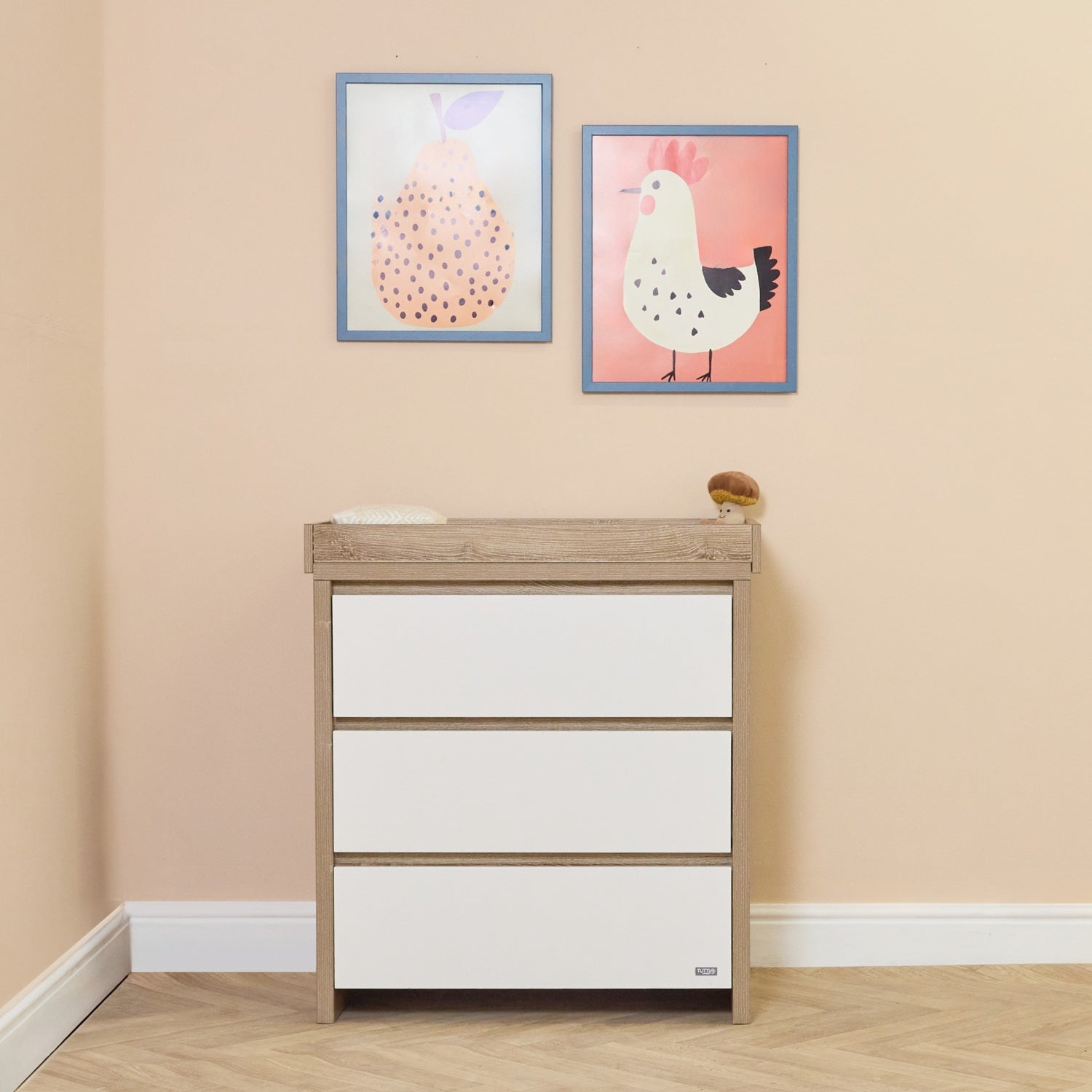 Lifestyle view of the Modena changing unit in white and oak, featuring three spacious drawers and a raised changing top for easy nappy time
