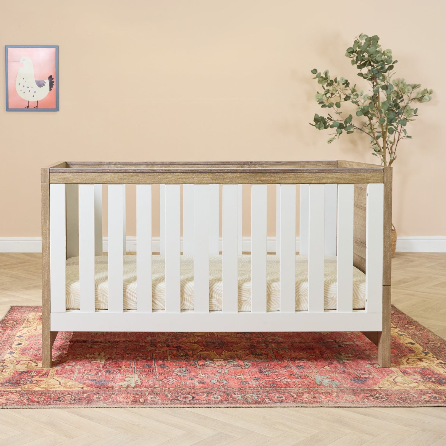 Modena 3-in-1 cot bed in white and oak styled in a warm nursery, showcasing its sturdy slatted sides and spacious sleeping area