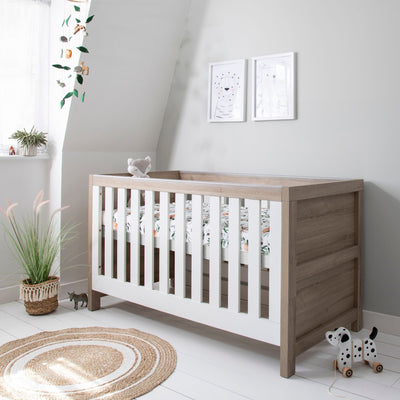 Nursery view of the Modena Cot Bed in White Oak in cot bed mode with woodland print bedding, styled in a light and modern room
