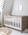 Nursery view of the Modena Cot Bed in White Oak in cot bed mode with woodland print bedding, styled in a light and modern room