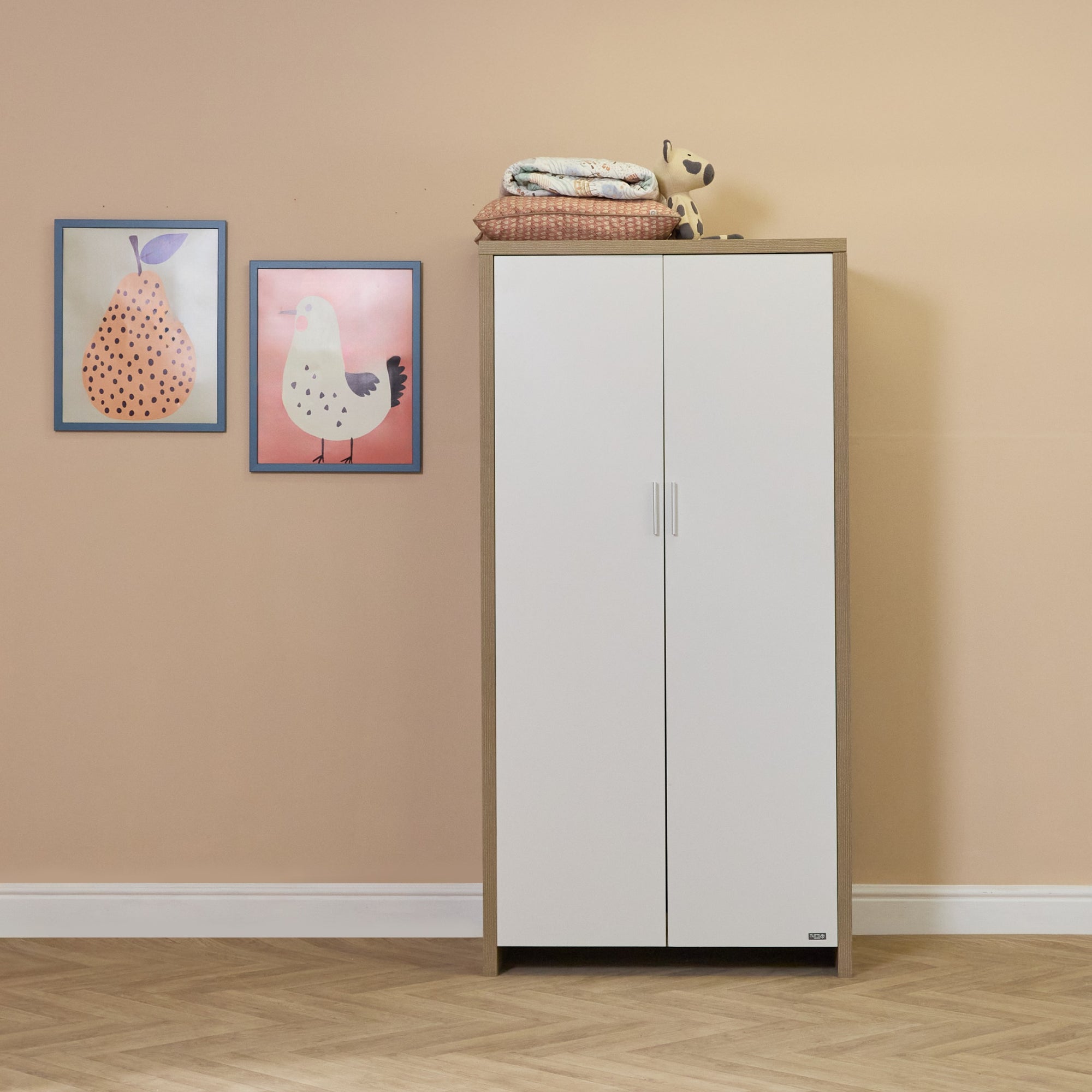 Lifestyle view of the Modena wardrobe in white oak, featuring clean white doors and ample storage, styled in a soft, neutral nursery setting