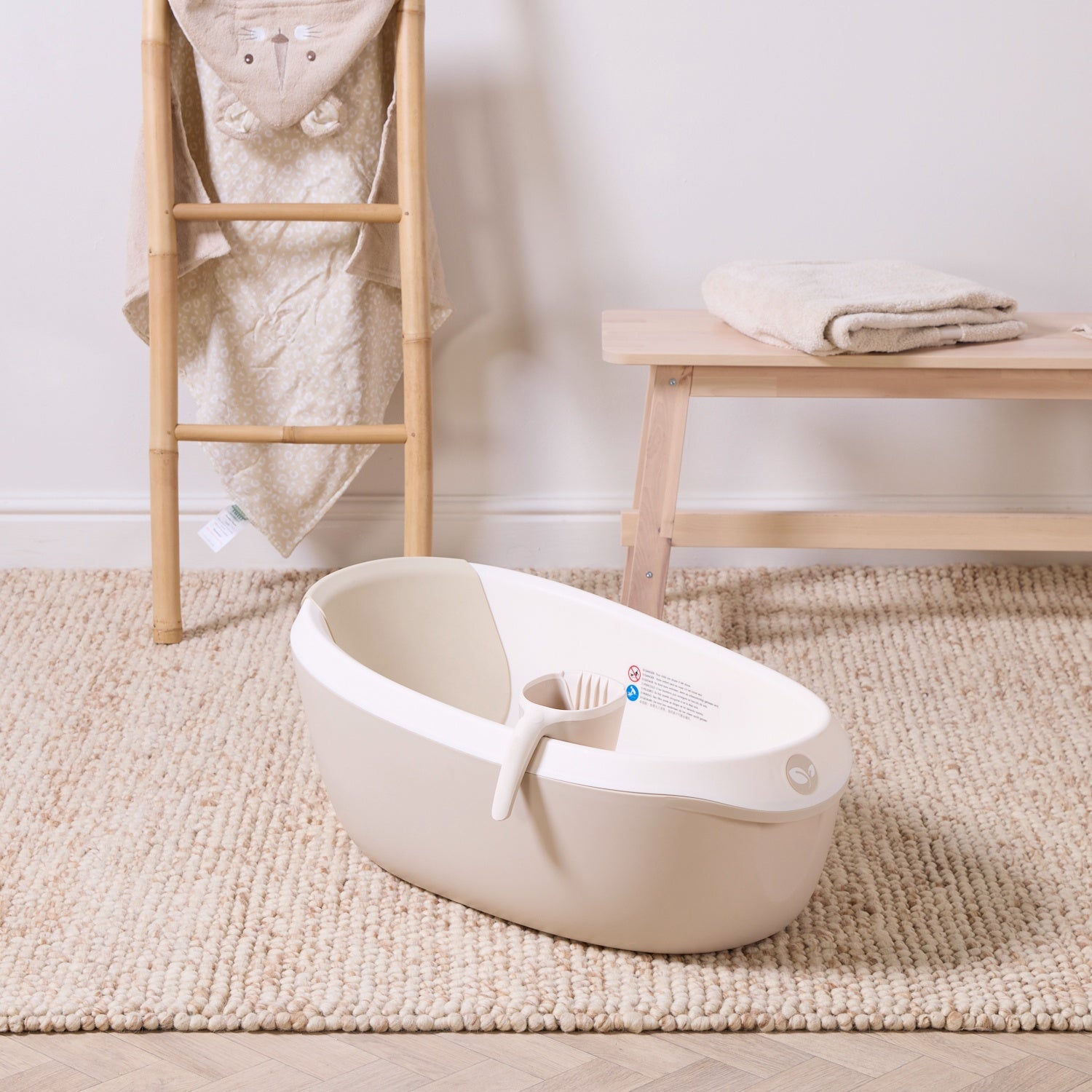Nati Baby Bath in dune with matching jug, styled on a soft woven rug with warm neutral nursery accessories nearby.