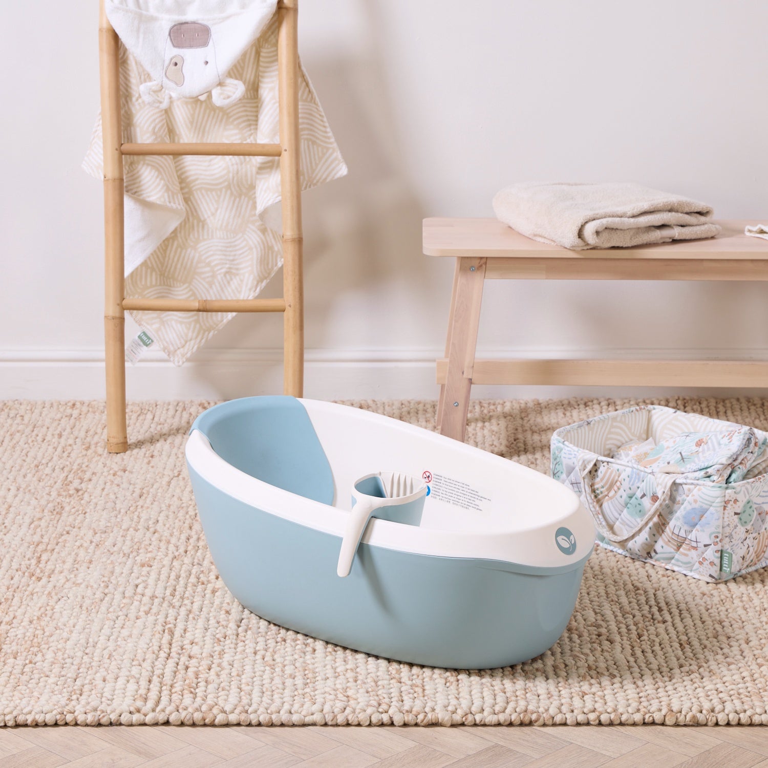 Nati Baby Bath in ocean with matching jug, styled on a soft nursery rug beside natural wood furniture and baby essentials.