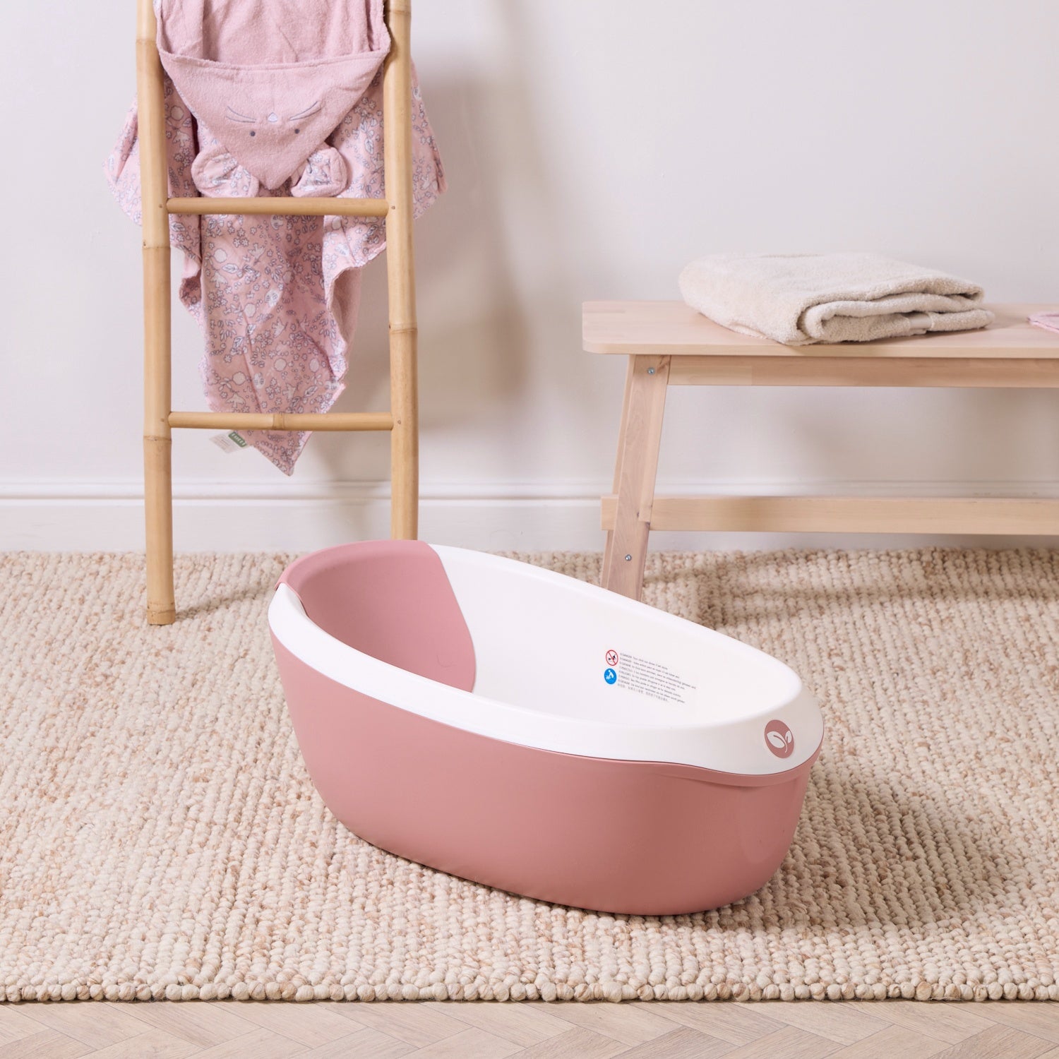 Nati Baby Bath in shell placed on a textured nursery rug, featuring a soft pink and white design in a calm bathroom setting.