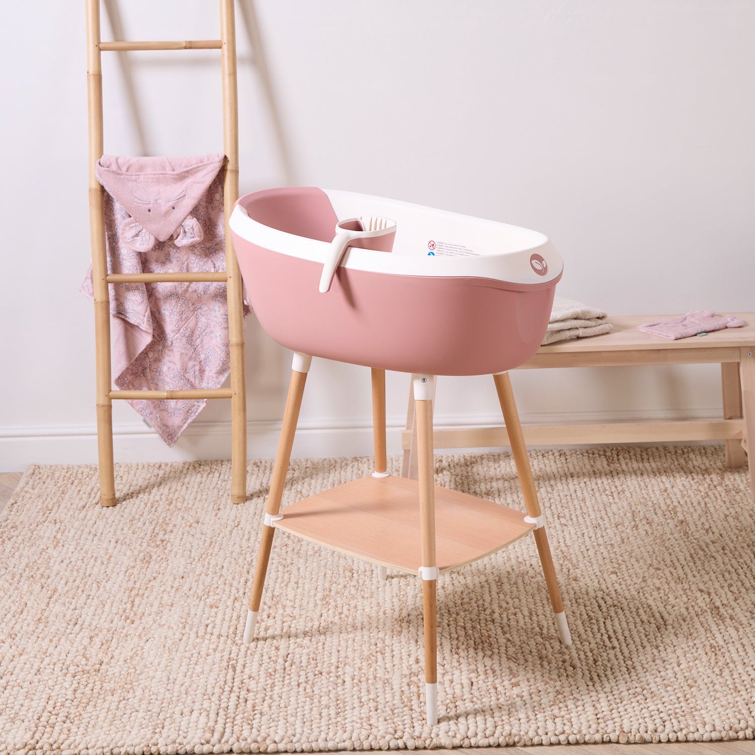 Nati Baby Bath in shell displayed on wooden stand with matching jug, showcasing elevated bathing setup and compact storage shelf.
