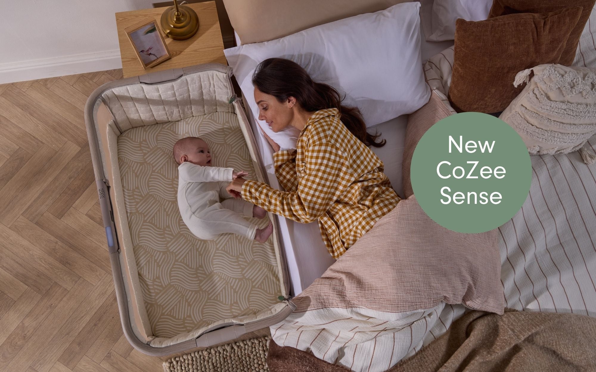 Woman interacting with a baby in a CoZee Sense crib next to a bed.