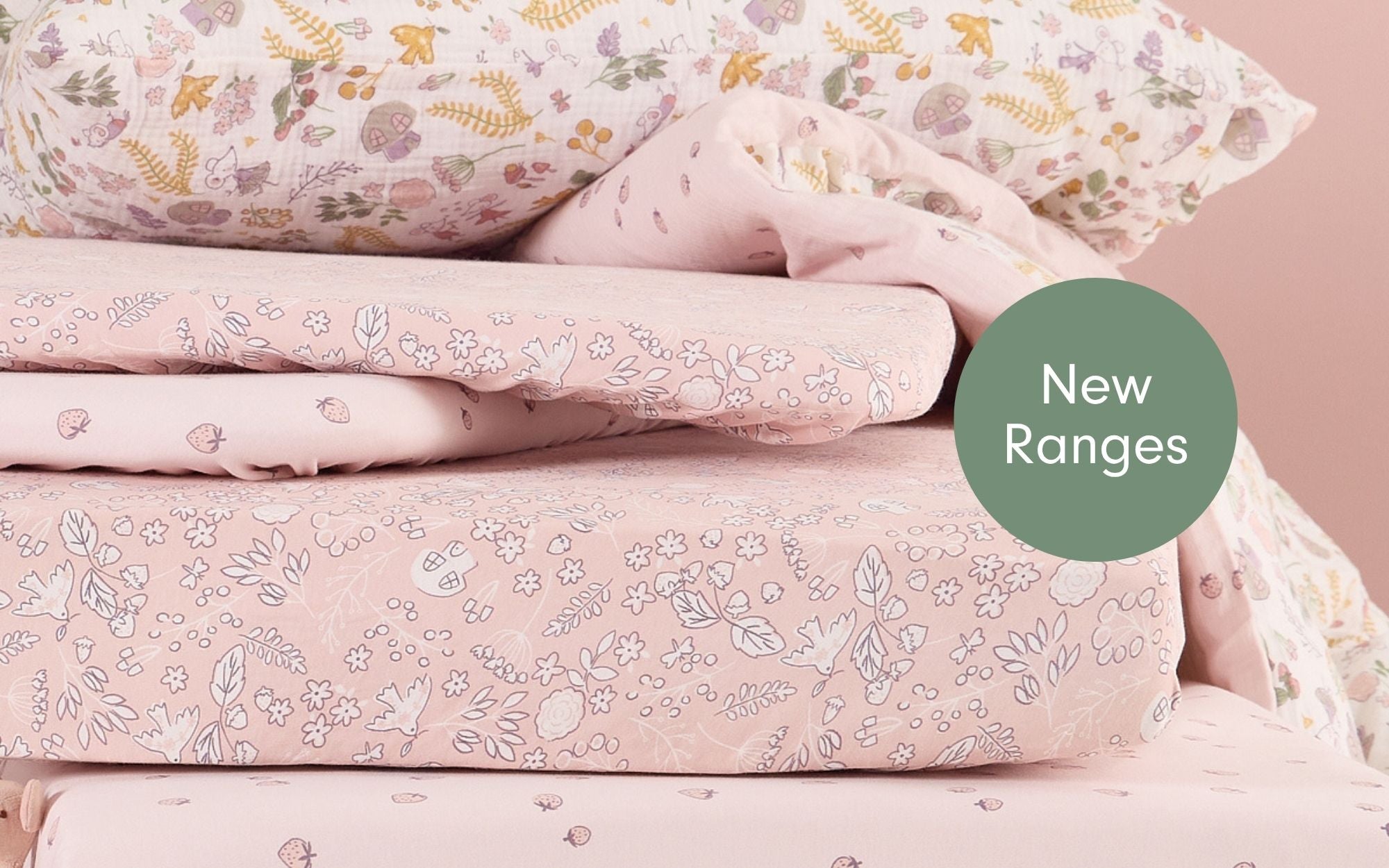 Stack of floral-patterned bedding from the Tiny Tails collection with a 'New Ranges' label on a pink background