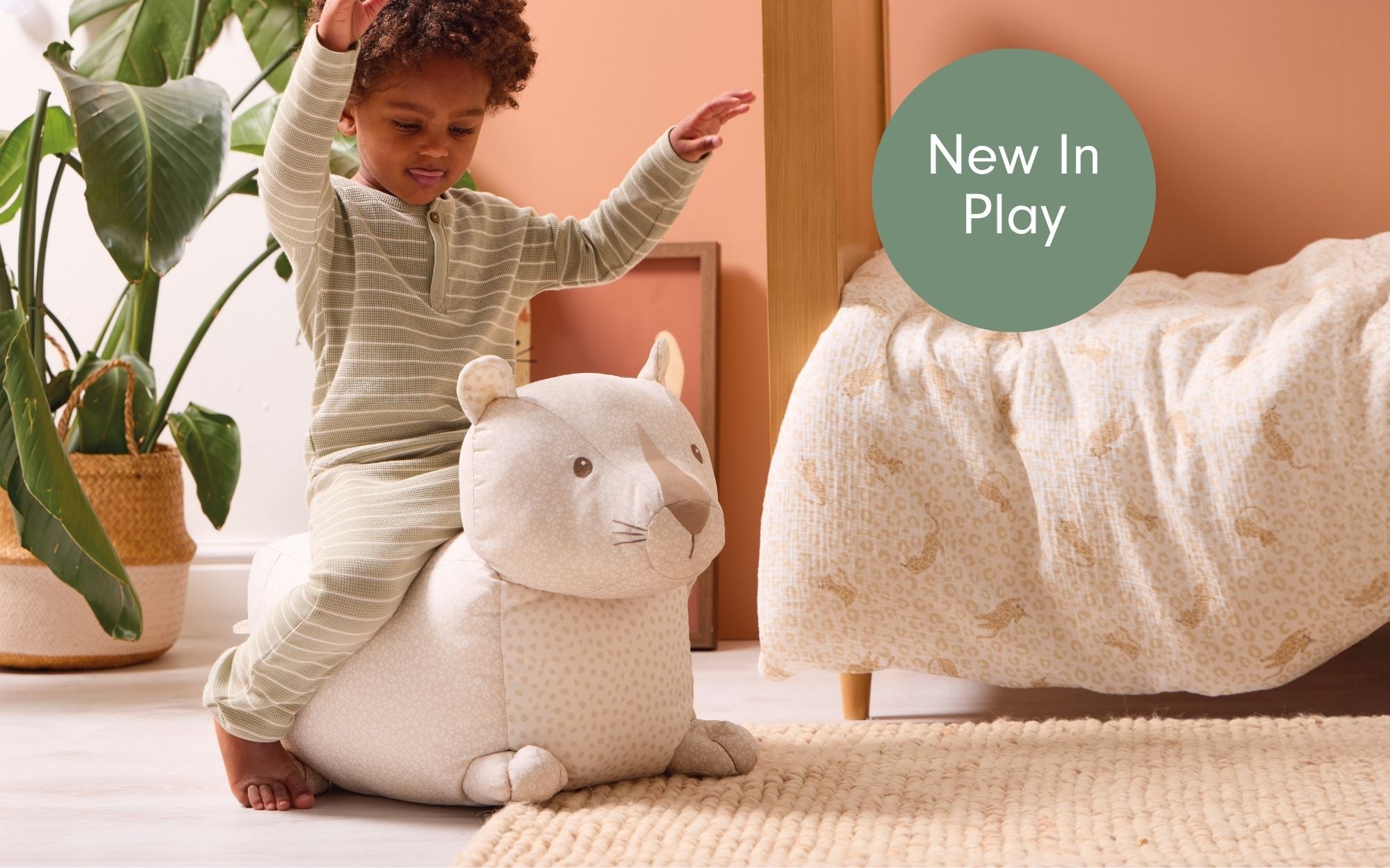 A child playing with a Larry Leopard ride-on on a light-colored floor with a plant and furniture in the background.
