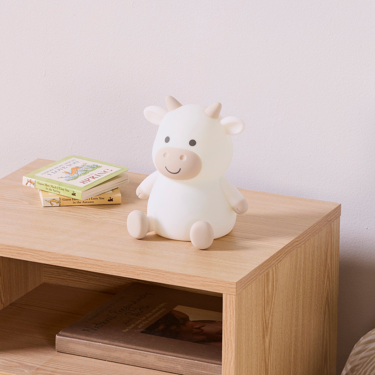 White and brown cow night light on a wooden surface with books in the background