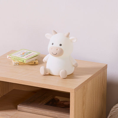 White and brown cow night light on a wooden surface with books in the background