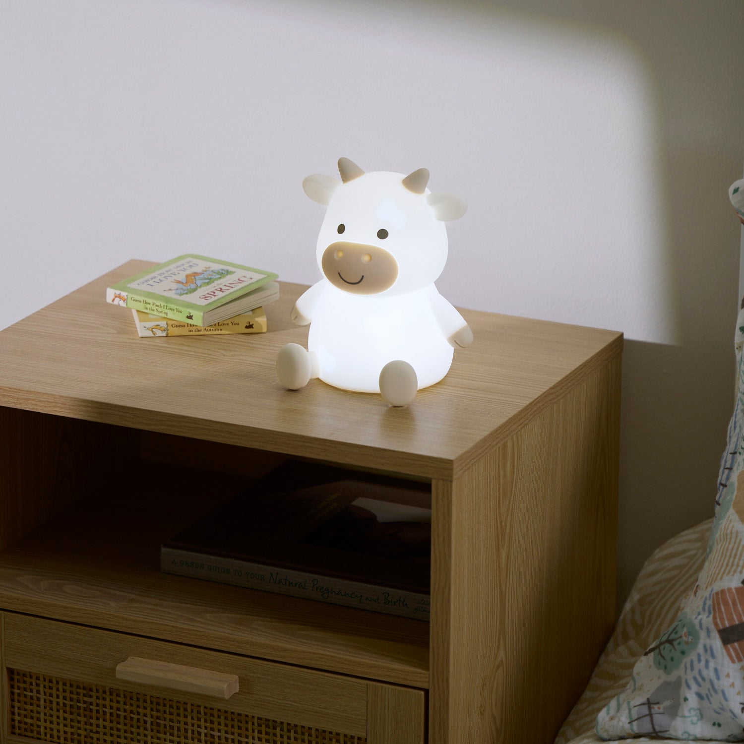 Cow-shaped night light on a wooden nightstand with books in the background