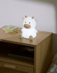 Cow-shaped night light on a wooden nightstand with books in the background