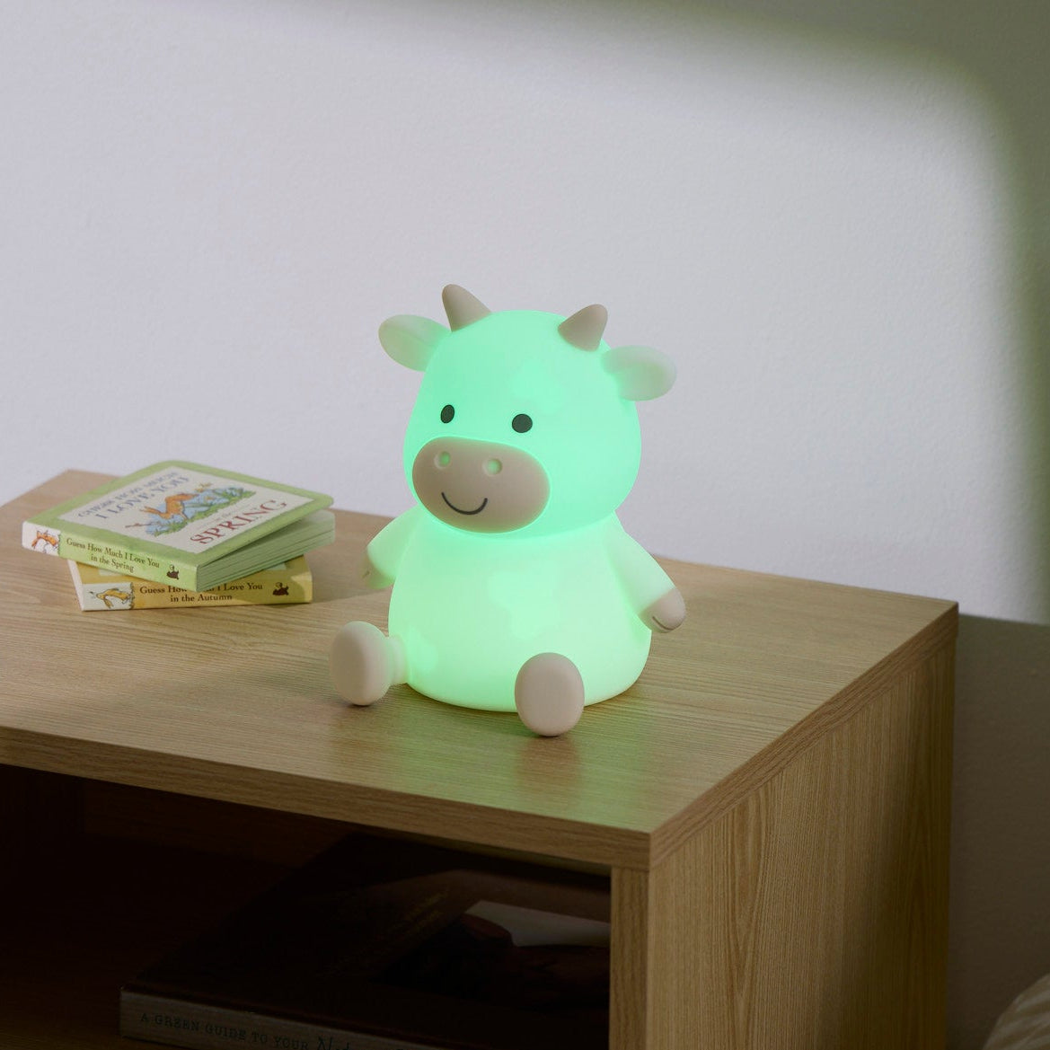 Glowing green cow-shaped night light on a wooden surface with books in the background.