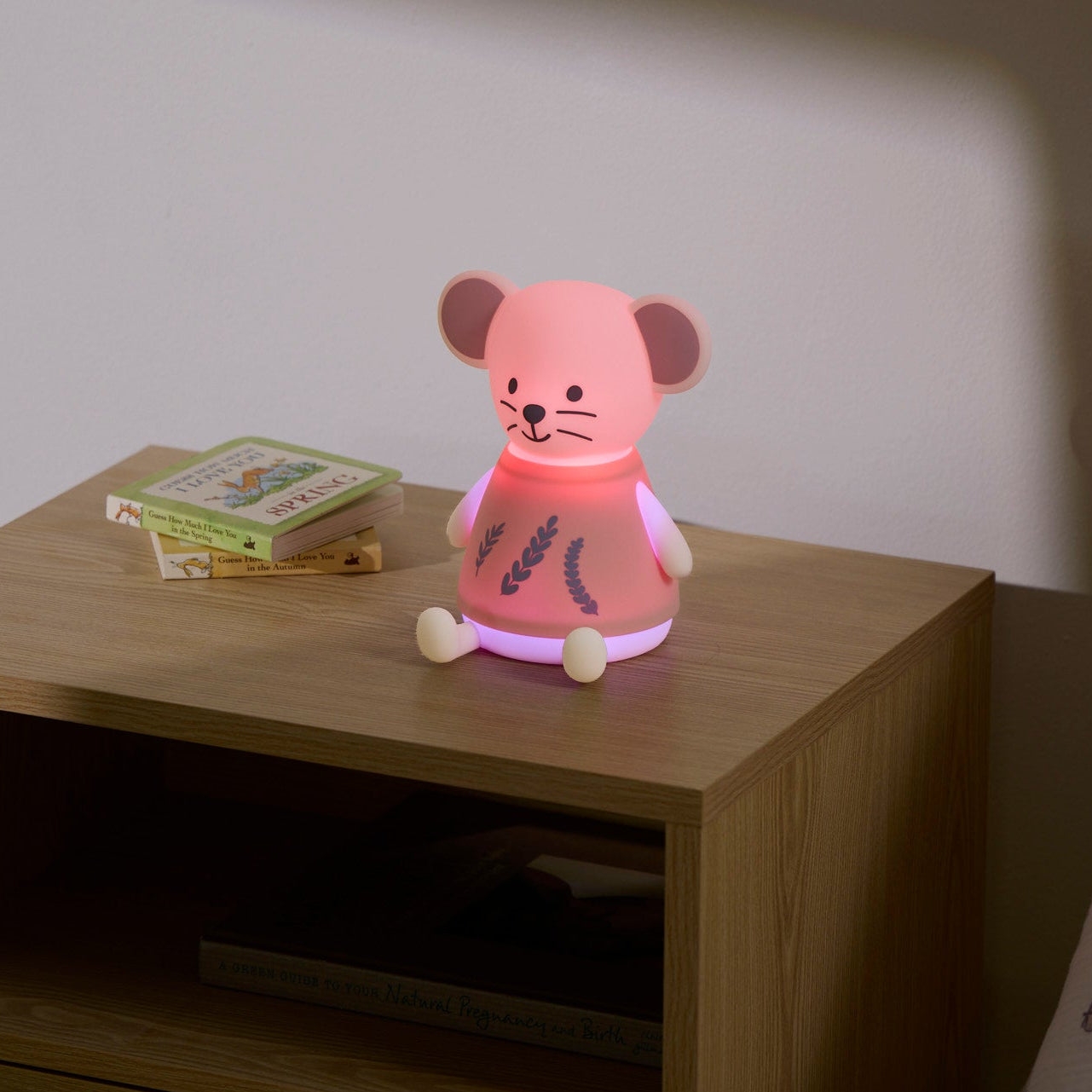 Pink mouse-shaped night light on a wooden nightstand with a book in the background.