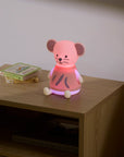 Pink mouse-shaped night light on a wooden nightstand with a book in the background.