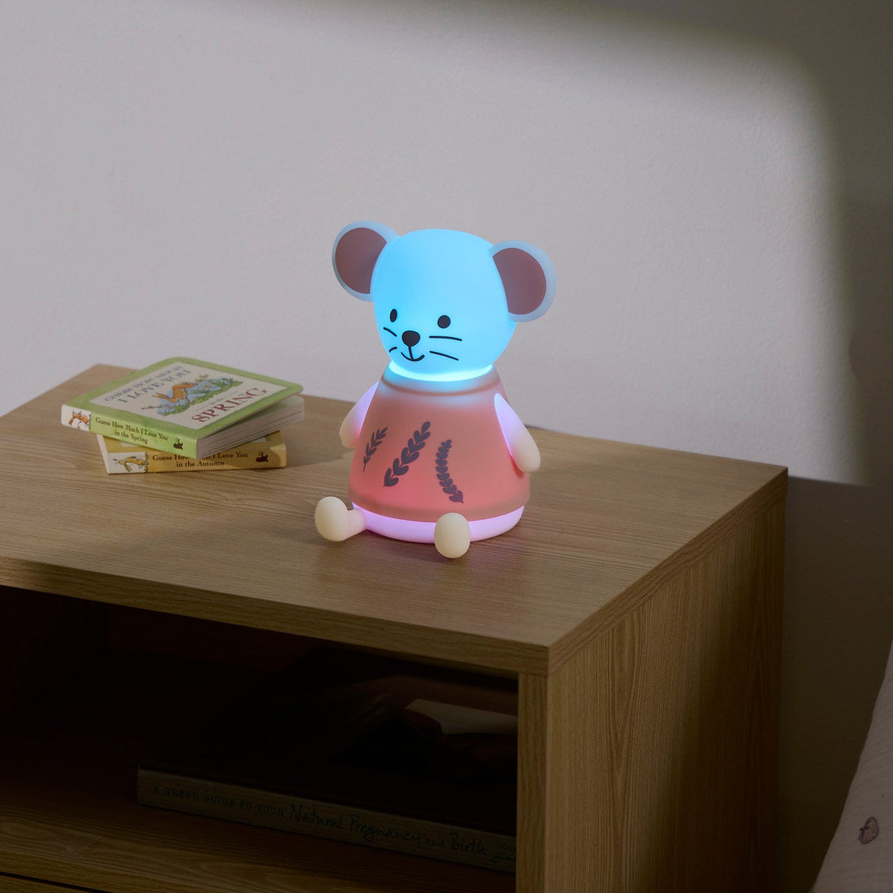 Children's night light shaped like a mouse on a wooden nightstand with a book in the background.